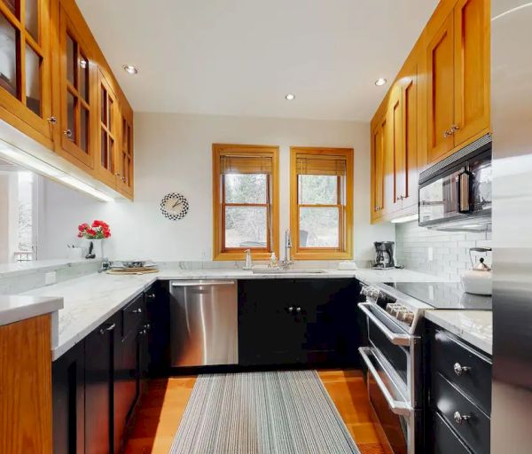 This image shows a modern kitchen with wooden cabinets, stainless steel appliances, a dishwasher, and a rug on the floor, featuring a cozy atmosphere.