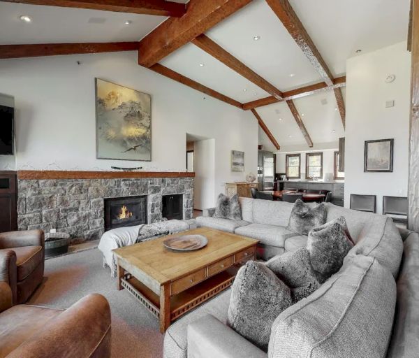 A spacious living room featuring exposed wooden beams, a stone fireplace, modern furnishings, and a spiral staircase leading upstairs ends the sentence.