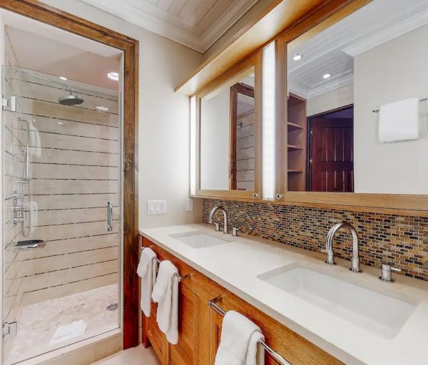 A modern bathroom with double sinks, a glass-enclosed shower, wooden cabinetry, and a large mirror with warm lighting.