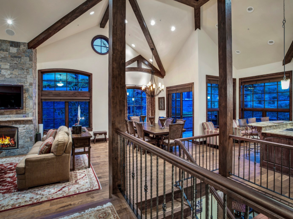 A spacious, open-concept living area with wood beams, a stone fireplace, large windows, a dining table, and a kitchen with a center island.